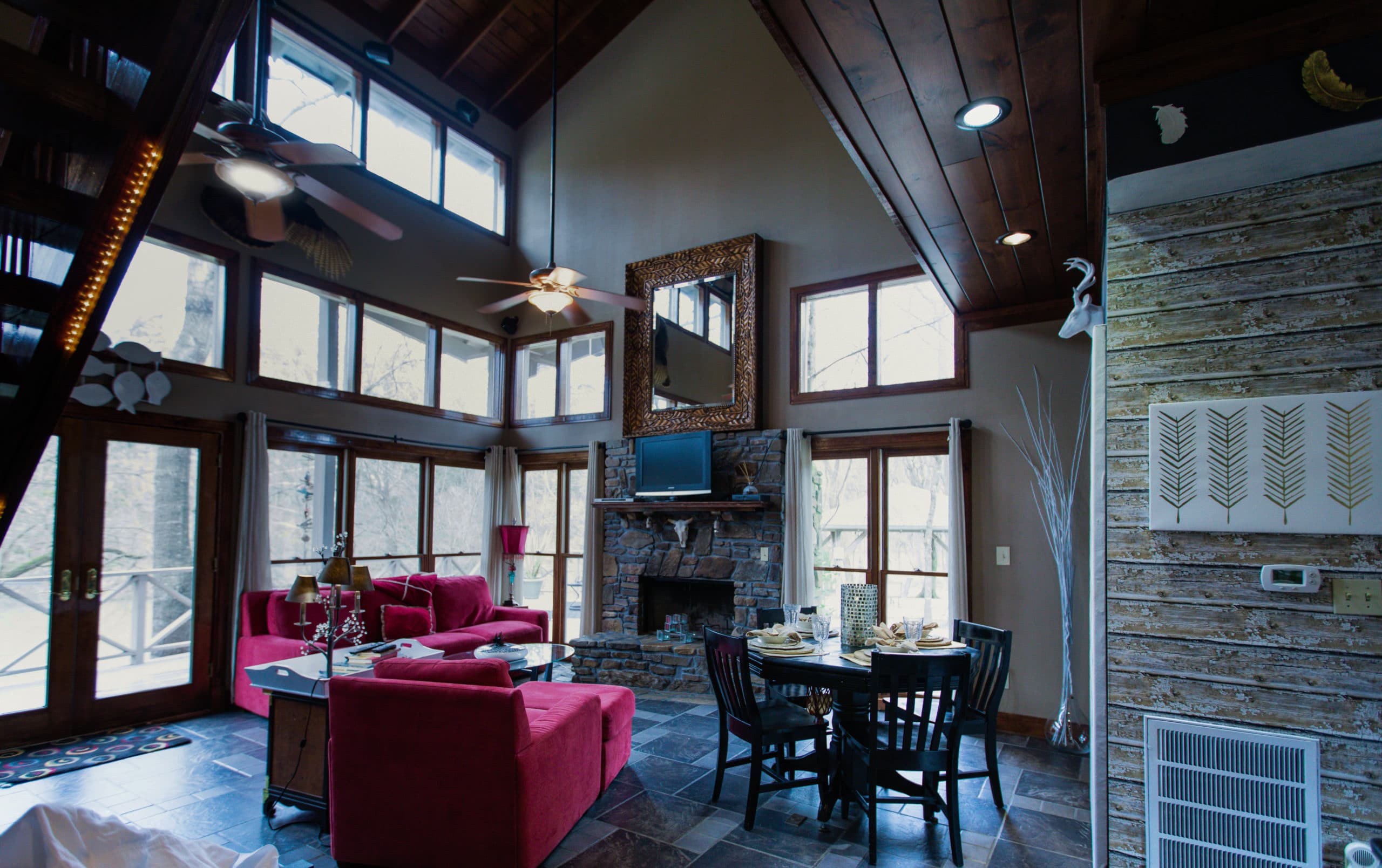 rivers-bend-cabin-04-riverside-retreat-living-room-wall-of-windows-fireplace-red-furniture-dining-table-standing-view-scaled
