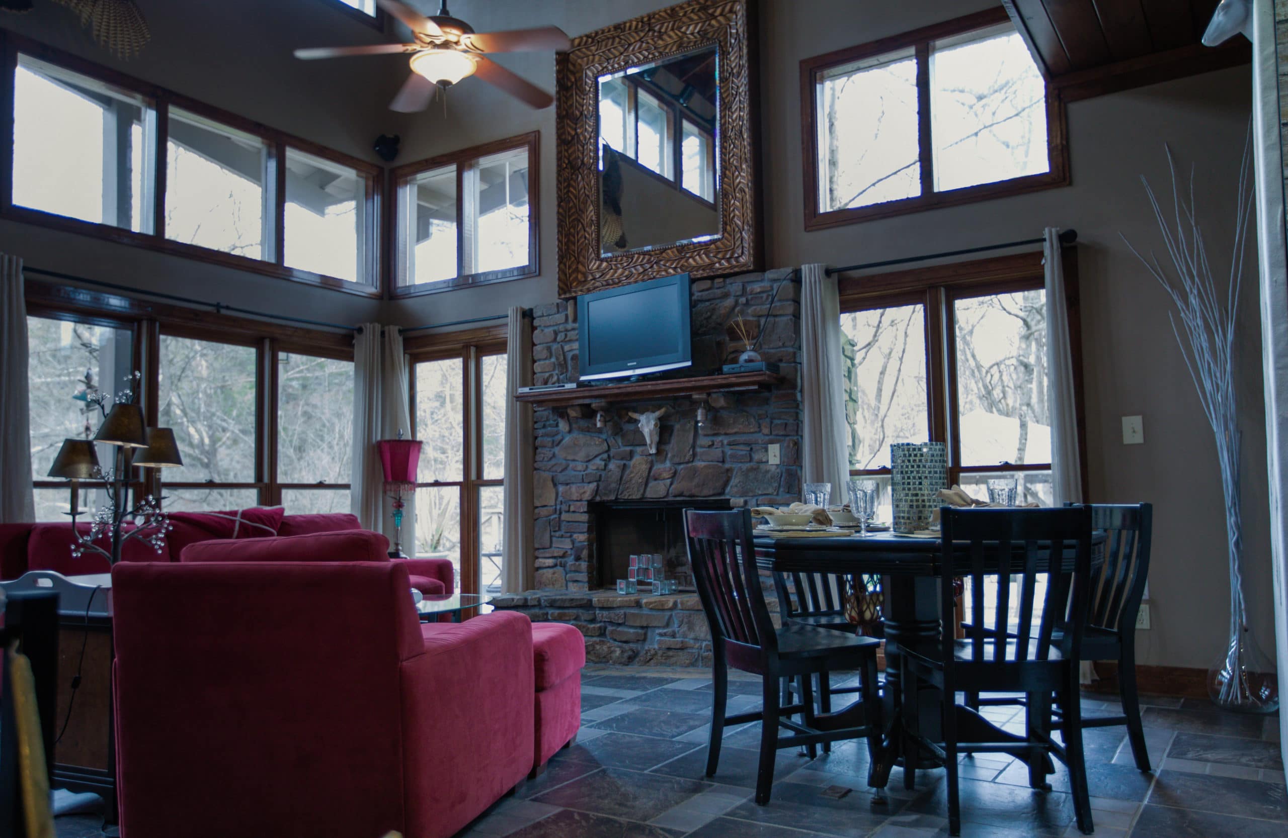 rivers-bend-cabin-04-riverside-retreat-living-room-wall-of-windows-red-furniture-dining-table-sitting-view-scaled